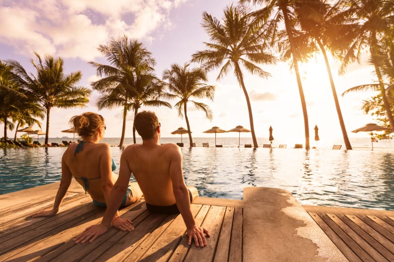 Ein Paar genießt ihren Strandurlaub in einem tropischen Resort mit Pool bei Sonnenuntergang ©NicoElNino/iStock