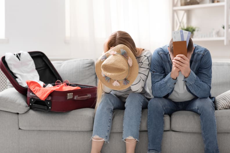 Paar sitzt traurig zu Hause in der Nähe von gepackten Koffer für den Urlaub ©iStock.com/Prostock-Studio