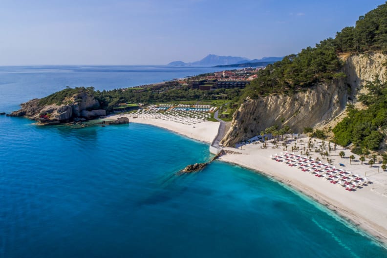 Strandabschnitt mit Felsen, Hotelgebäude und Meerblick im Maxx Royal Kemer Resort an der Türkischen Riviera