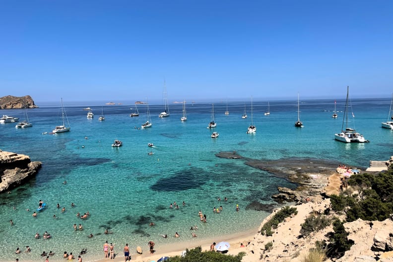 Boote und Touristinnen an der Cala Comte, Ibiza, Spanien