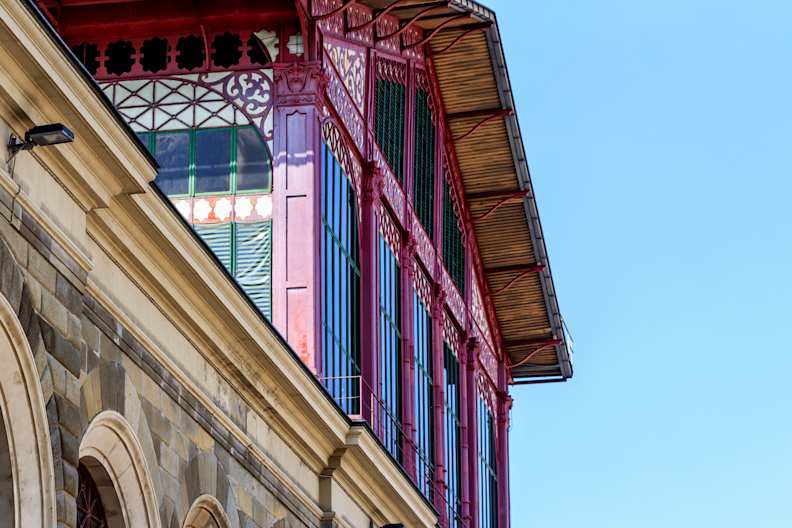Man sieht den oberen Teil der Markthalle in Florenz. Das Gebäude ist mit Schnörkeln in den farben Lila und fuchsia verziert und hat große Glasfenster.