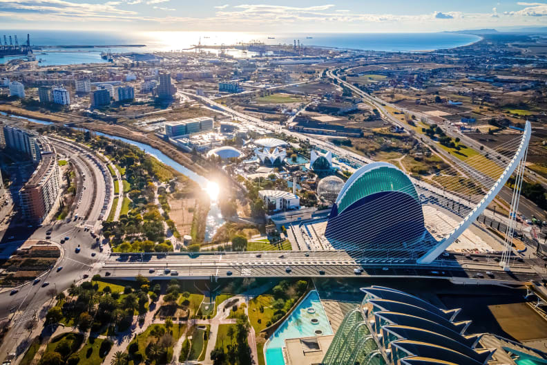 Drohnenfoto über die außergewöhnlich geformten Gebäude der Ciudad de las Artes y Sciencias. Das Viertel hat viele Grünanlagen. In der Ferne sieht man das Meer