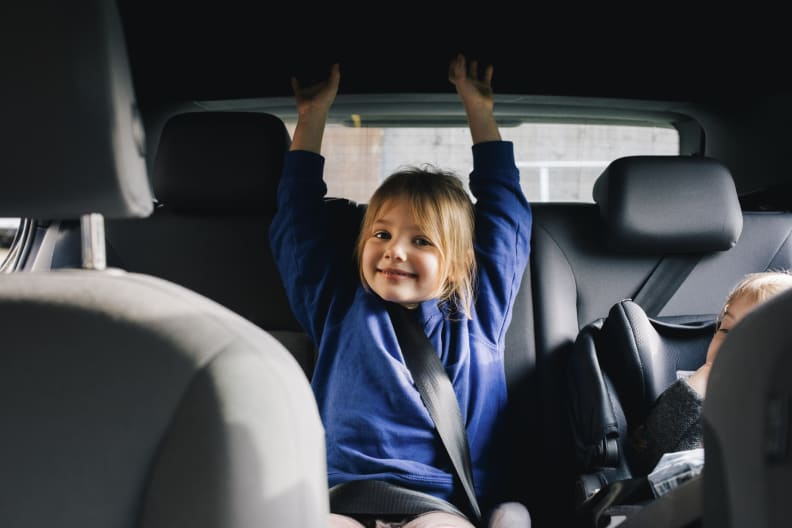 Ein kleines Mädchen sitzt fröhlich auf der Rückbank eines Autos. © Maskot/Maskot via Getty Images