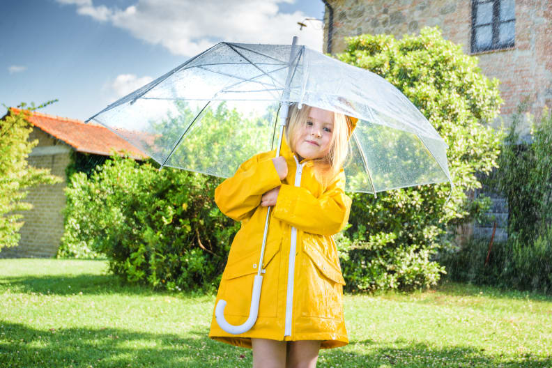 Ein Mädchen mit einem gelben Regenmantel unter einem Regenschirm.