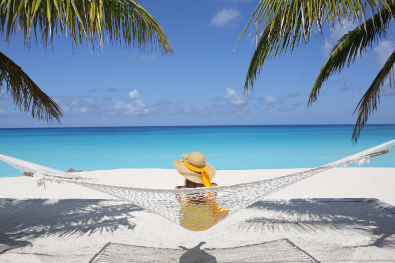 Eine Frau sitzt auf einer Hängematte an einem Paradiesstrand.