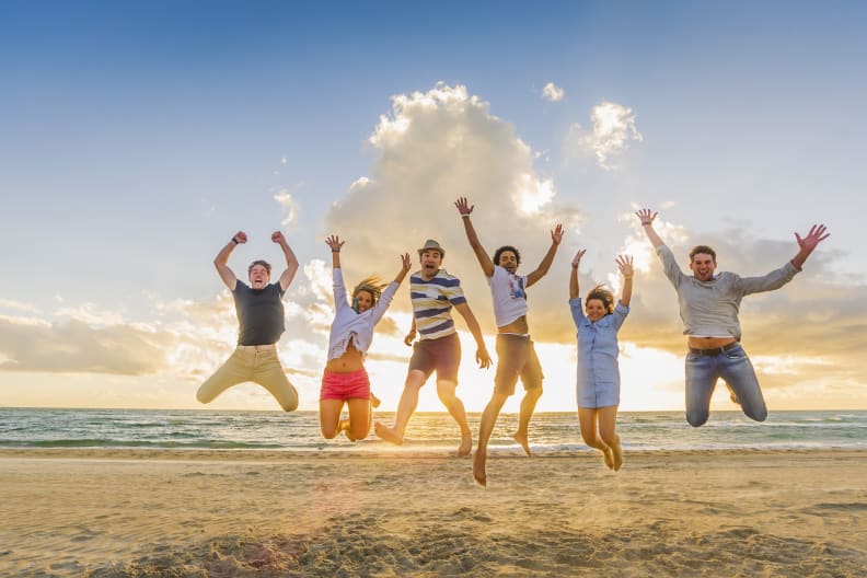 Eine Gruppe von FreundInnen springt an einem Strand in die Luft.