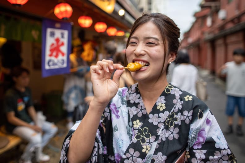 Eine junge Frau ist Dango Knödeln auf der Straße in Tokyo.
