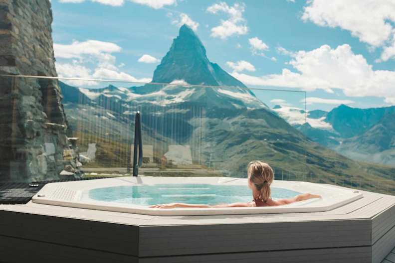 Eine Frau entspannt in einem Whirlpool mit Blick auf die umliegende Berglandschaft.