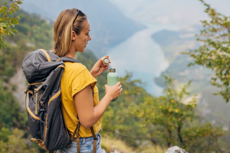 Eine Frau schließt ihre Wasserflasche aus Stahl und genießt den Ausblick von einem Gipfel.