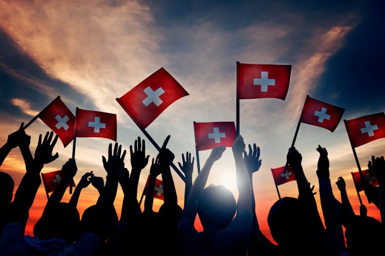 Eine Gruppe Menschen schwenkt viele kleine Schweiz Flaggen im Sonnenuntergang