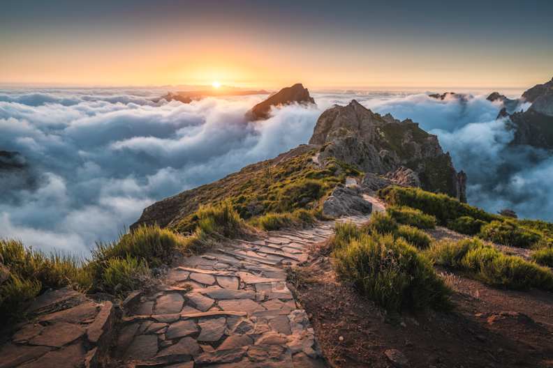 Gepflasterter Fußweg am Pico do Arieiro über den Wolken zum Sonnenaufgang, Madeira. © Marco Bottigelli via Getty Images