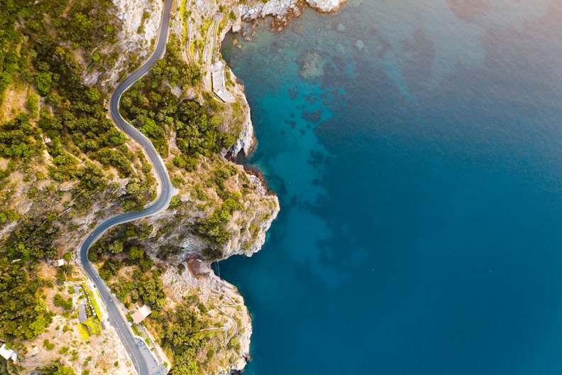 Dronenblick auf die Küstenstraße und tiefblaues Meer an der Amalfiküste, Italien. © Marco Bottigelli via Getty Images