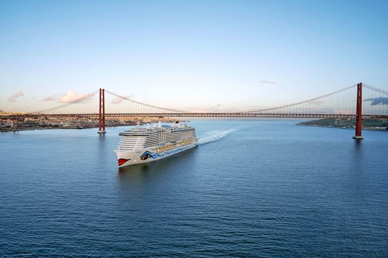 Ein Kreuzfahrtschiff fährt unter einer Brücke hindurch.