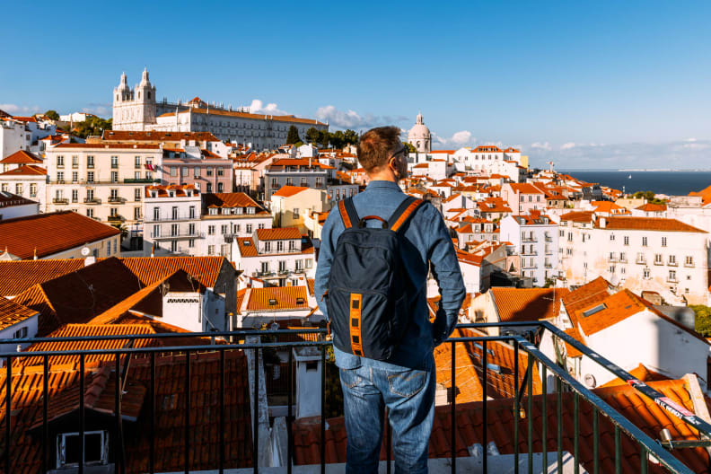 Ein Mann steht mit einem Rucksack vor der Altstadt von Lissabon.