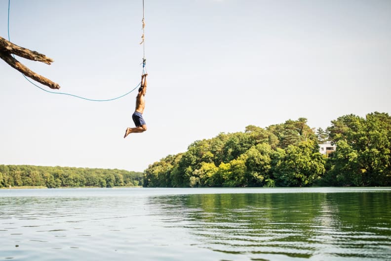 Ein Mann springt an einer Liane ins Wasser.