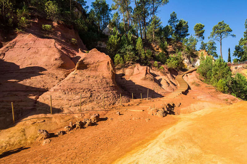 Ein ockerfarbener Wanderweg mit Bäumen im Hintergrund in Roussillon in Frankreich.