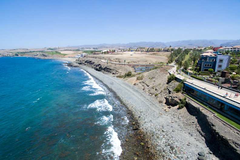 Blick auf den Playa de las Mujeres. Zu sehen ist der kieselige Strand, die Promenade und das Meer.