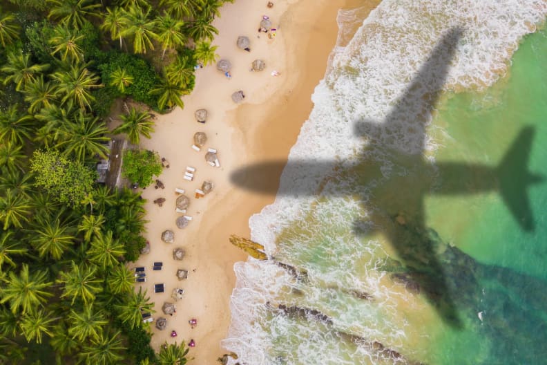 Die Silhouette eines Flugzeugs über einem tropischen Strand.