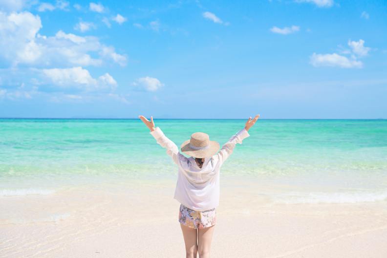 Eine Frau steht mit ausgebreiteten Armen am Meer.