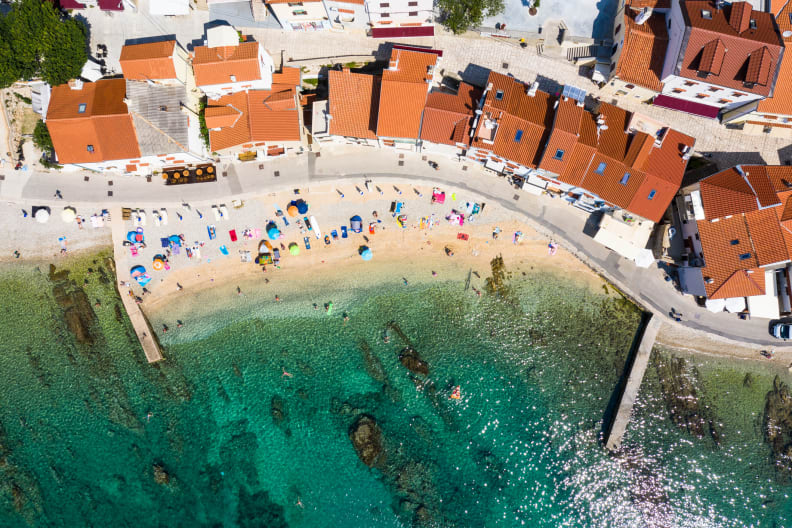 Strand mit Urlauberinnen direkt an einer Häuserreihe auf Krk, Kroatien.