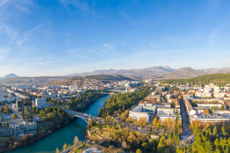 Drohnenausblick über eine Stadtkulisse. Im Hintergrund sieht man eine Bergkulisse.