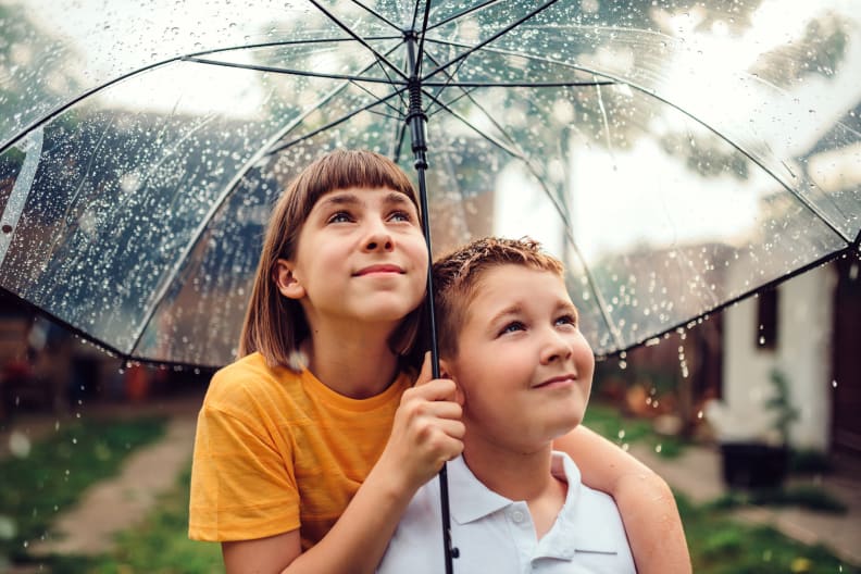Zwei Kinder stehen gemeinsam unter einem Regenschirm. © Kerkez/iStock / Getty Images Plus via Getty Images