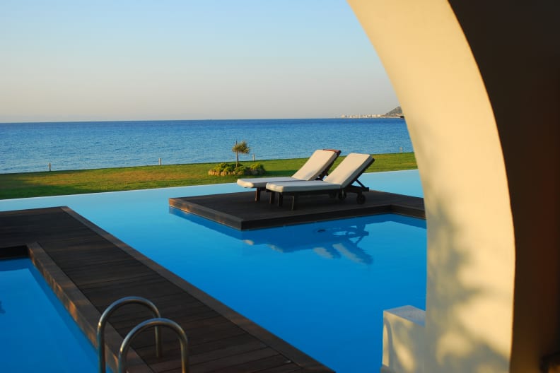 Zwei Sonnenliegen an einem Pool mit Meerblick auf Rhodos, Griechenland.