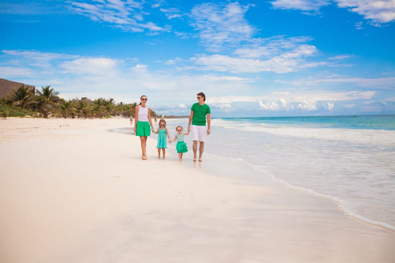Mutter, Vater und zwei kleine Kinder laufen an einem wunderschönen Strand am Meer entlang.
