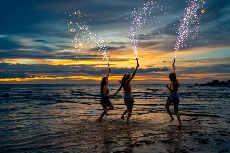 Drei Frauen springen ins Meer mit Silvesterfontänen und haben Spaß