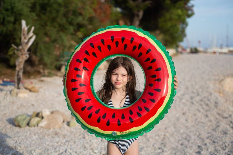 Mädchen hält einen Schwimmring in Melonen-Optik an einem Strand in Kroatien hoch.