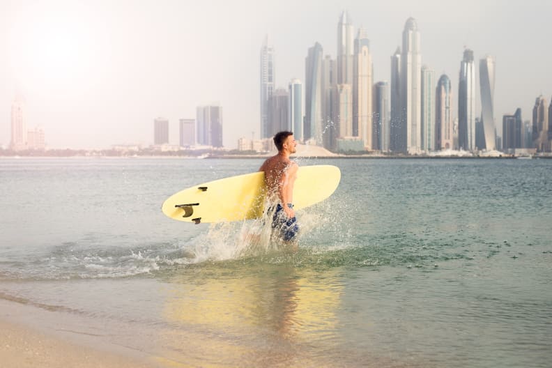 Surfer läuft ins Wasser vor der Hochhaus-Kulisse von Dubai.