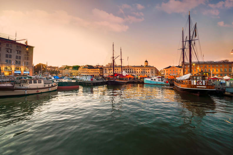 Ein Hafen bei Sonnenuntergang. Mehrere Boote liegen im ruhigen Wasser, die Promenade ist mit Lichterketten dekoriert.