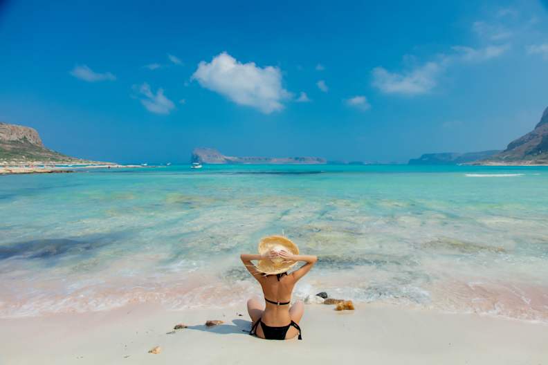 Mädchen im schwarzen Bikini und mit Hut am Strand von Balos © GettyImages