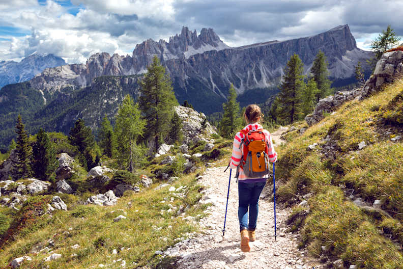 Eine Frau wandert auf einem schmalen Wanderweg vor einer spektakulären Bergkulisse in den Dolomiten in Südtirol, Italien ©shutterstock_1140667871