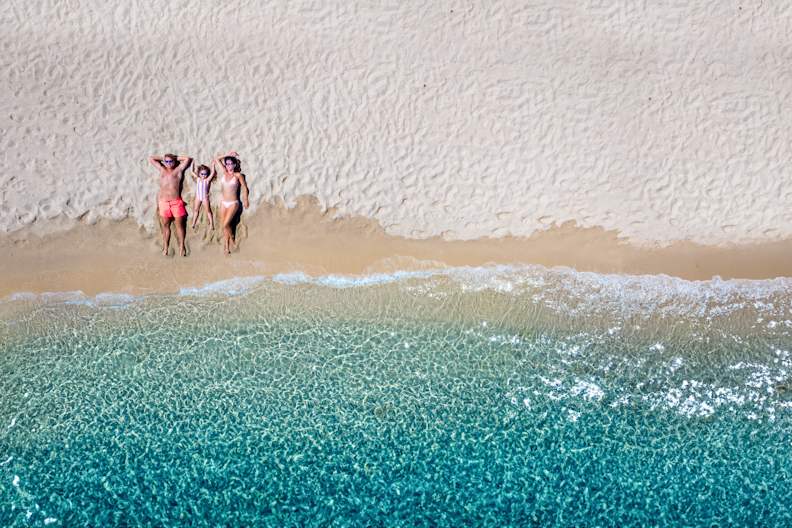 Dreiköpfige Familie liegt am Strand und genießt die Sonne im Familienurlaub © Shutterstock