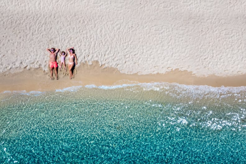 Vater, Mutter und Kind liegen an einem Strand am Meer.