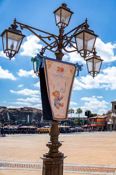 Ein Platz mit bunten, ästhetischen Häusern am Rand, einer verschnörkelten Laterne im Vordergrund und im Hintergrund Berge mit kleinen Wasserfällen im DisneySea bei Tokyo, Japan.