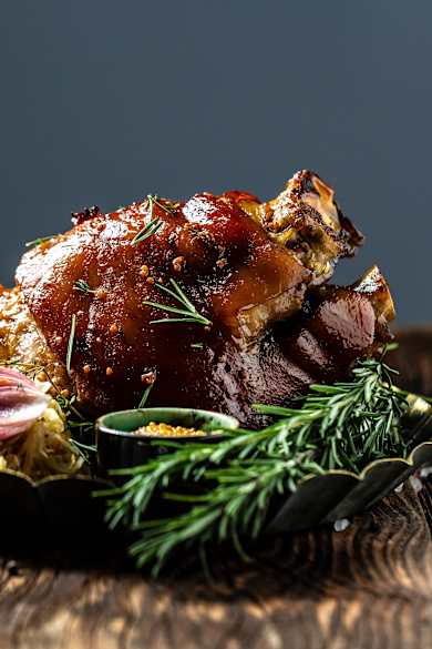 Zartes Eisbein mit Kraut und Senf in einer Schale mit Rosmarin auf einem rustikalen Tisch.