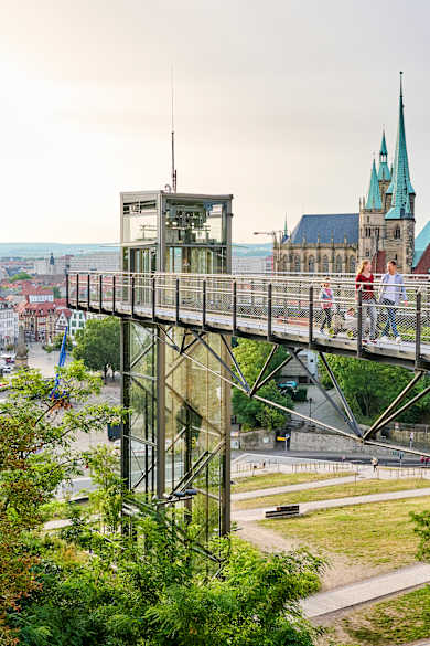 Ein Skywalk führt über einen Park, im Hintergrund liegt eine Kathedrale und eine Innenstadt mit historischen Fassaden