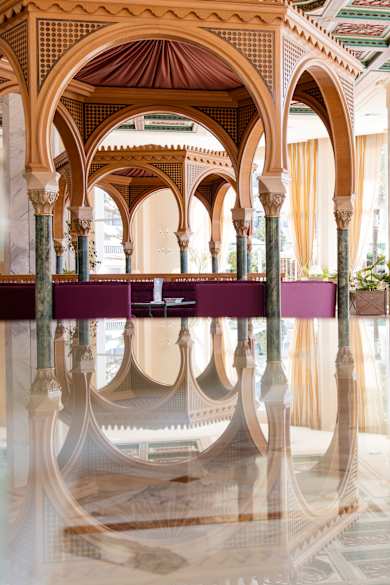 Das Bild zeigt ein modern eingerichtetes Wellnesszentrum. Der Blick geht über eine glatte Wasserfläche auf eine hölzerne Pagode. Die Fenster sind groß und an den Raumwänden stehen Blumen