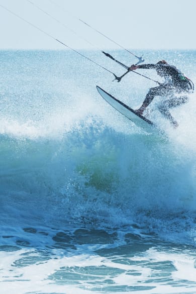 Kitesurfer springt über eine schäumende Welle © iStock.com/shaunl