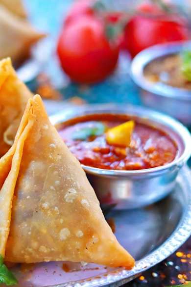 Mehrere Samosas liegen auf einem silbernen Teller mit einer kleinen Soßenschale.