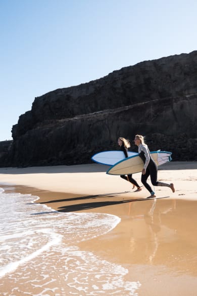 Surferinnen am Strandufer rennen zu den Wellen © iStock.com/1MEDIA