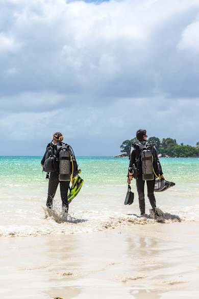 Zwei Taucher mit Ausrüstung laufen am Strand auf ein Boot zu