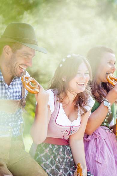 Drei Frauen und zwei Männer in Dirndl und Lederhosten drinken Bier und essen Brezeln.