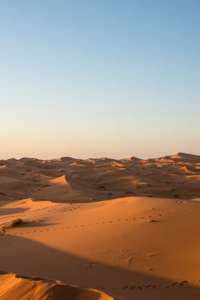 Ein Kind steht mit einem Fernglas auf einer Sanddüne in der Wüste Marokko.