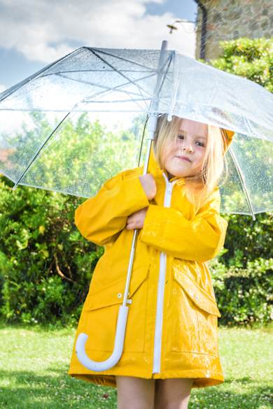 Ein Mädchen mit einem gelben Regenmantel unter einem Regenschirm.