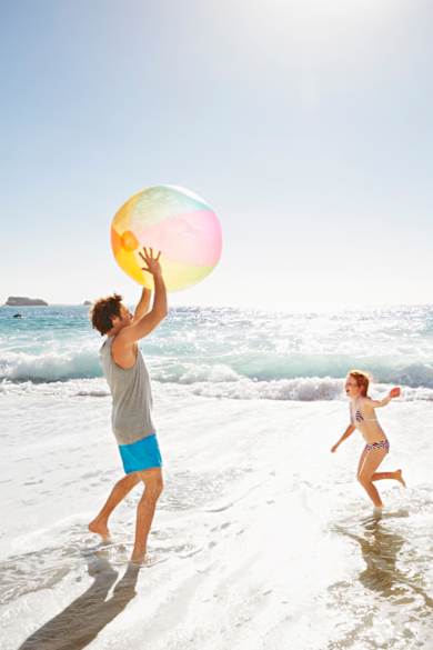Eine Familie spielt mit einem Wasserball am Meer.