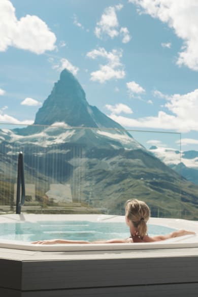 Eine Frau schaut von einem Whirlpool auf die Berge.