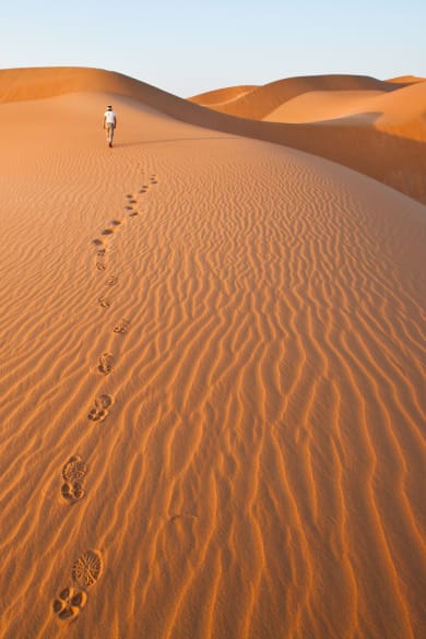 Eine Person läuft durch die Wüste und hinterlässt Fußspuren im Sand.